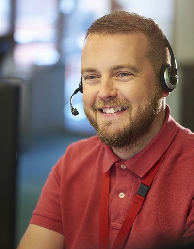 A man with a beard and a red t shirt smiling while using a headset